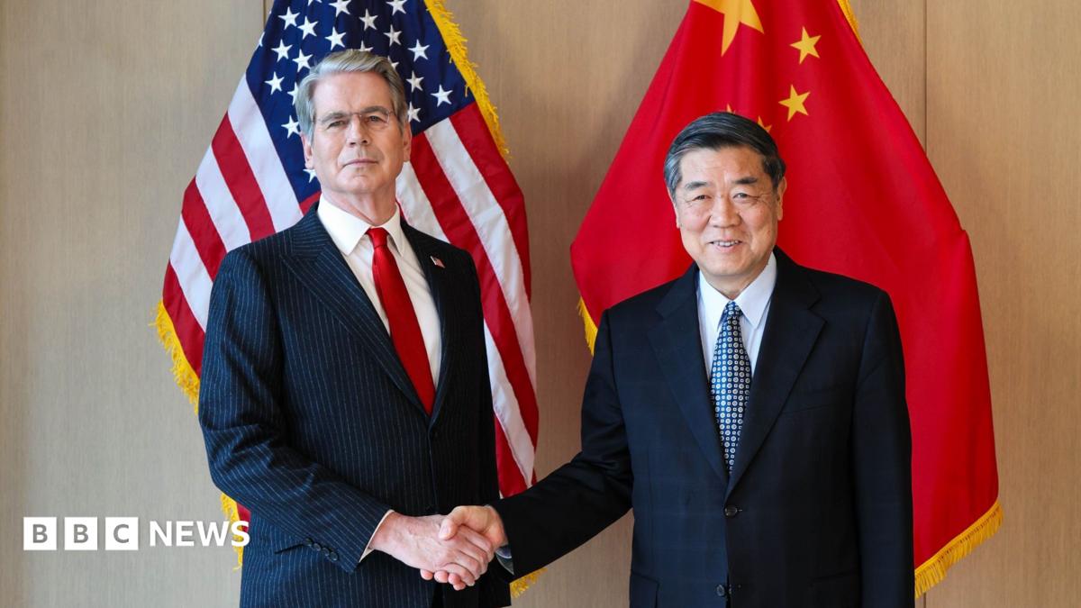 US Treasury Secretary Scott Bessent shakes the hand of China's top trade negotiator He Lifeng stand in front of both countries' flags.