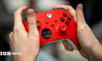 A close up of someone's hands holding a red Xbox controller