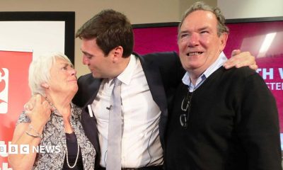 Andy Burnham hugs his parents, Eileen and Roy, after he was selected as the Labour candidate to become the mayor of Greater Manchester in September 2026. They are standing in front of a red banner reading "Labour North West".