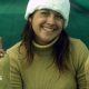 A woman smiles into the camera making peace signs with both hands
