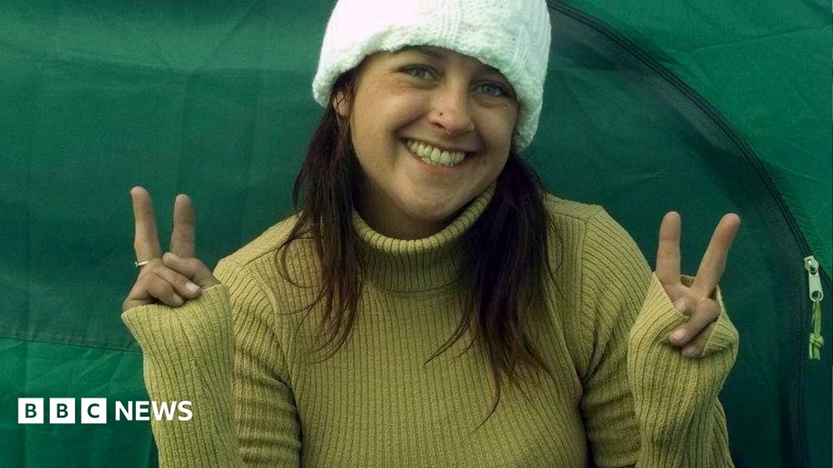 A woman smiles into the camera making peace signs with both hands