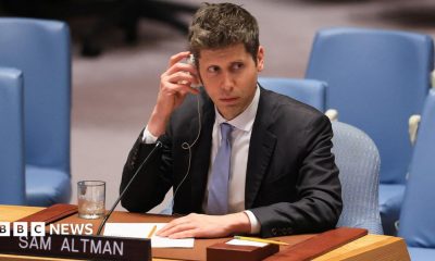 Sam Altman of OpenAI sitting before the US Security Council wearing a suit and tie while listening to a translation of comments.