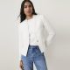 A woman wearing a white blazer, white top, and blue jeans