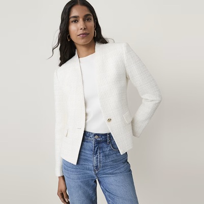 A woman wearing a white blazer, white top, and blue jeans