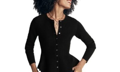 A woman wearing a black peplum cardigan, blue jeans, and gold necklaces