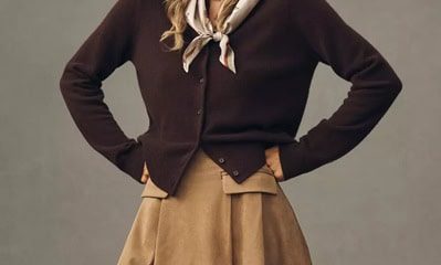 A woman wearing a dark brown cardigan, dark khaki colored skirt, and a multicolored scarf tied around her neck