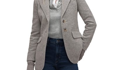 A woman wearing a gray polo shirt, gray blazer, and dark blue jeans