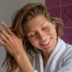 Portrait of young beautiful woman in a bathroom performing cosmetic procedures after bathing. Female wearing bathrobe, applying haircare product and smiling. Close up, copy space background.