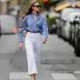 Segolene Hyppolite wears sunglasses, a blue and white oversized shirt from Tommy Hilfiger, a raffia beige bag from Vanessa Bruno, high waist white denim pants from Vanessa Bruno, Chanel slingback shoes in blue denim with black tips, during a street style fashion photo session, on May 20, 2024 in Paris, France.
