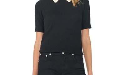 A woman wearing black pants and a black sweater with ivory scalloped trim at the neckline