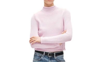 A woman wearing a light pink sweater, sunglasses, a black belt, and blue jeans