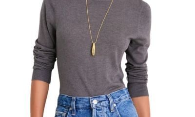A woman wearing a gray sweater, blue jeans, and a gold necklace with pendant