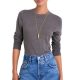 A woman wearing a gray sweater, blue jeans, and a gold necklace with pendant