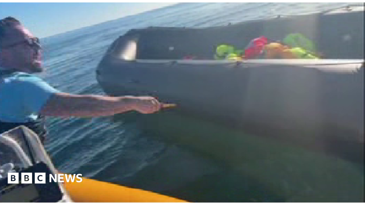 Anti-migrant campaigner leaning out of a boat appearing to hold a knife and to be shouting
