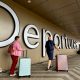 A man and a woman roll pink and blue suitcases past a large "Departures" sign at Belfast airport.