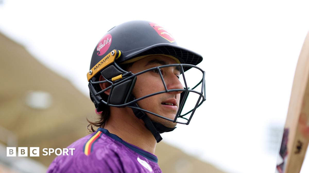 Robin Das wearing a black cricket helmet, carrying a cricket bat and wearing a purple top