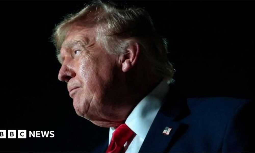 Donald Trump is wearing a navy suit jacket with a white shirt and a bright red tie.