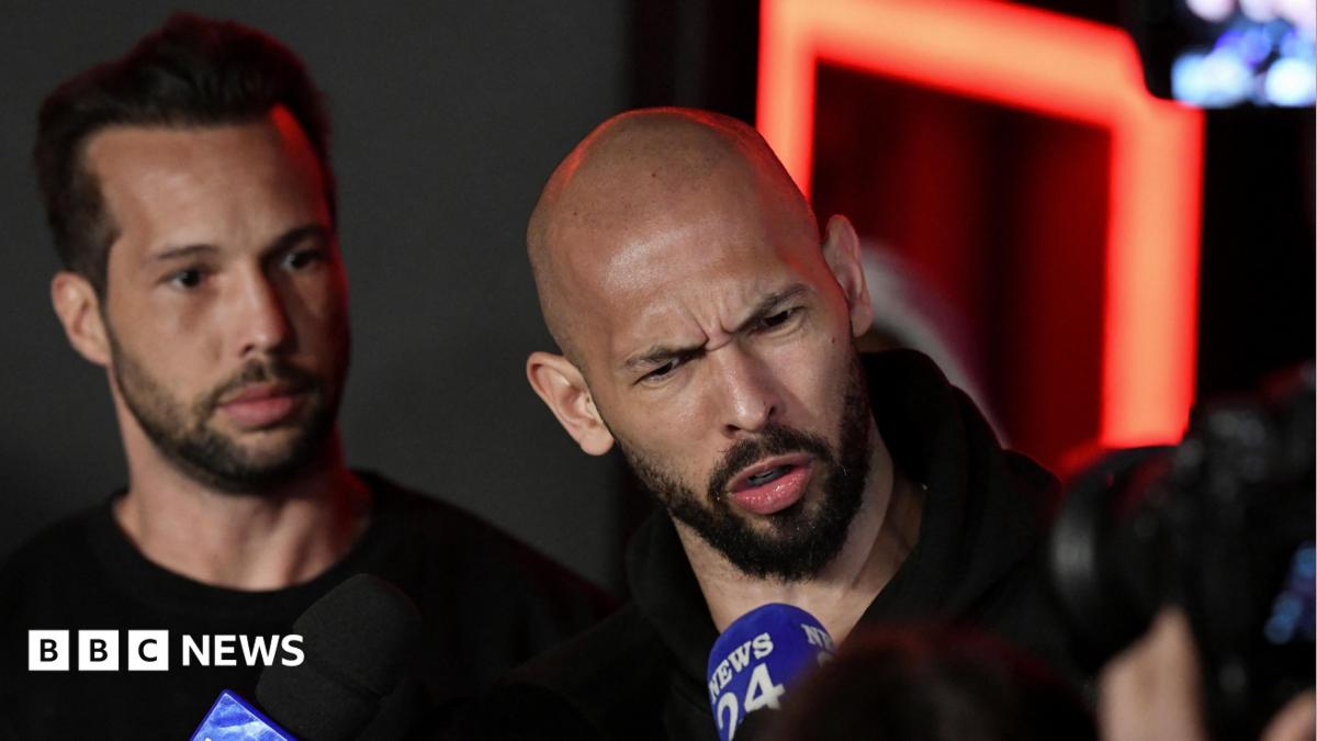 Tristan and Andrew Tate delivering a press statement. The brothers are dressed in black and Andrew has a disgruntled facial expression as he speaks into a microphone.