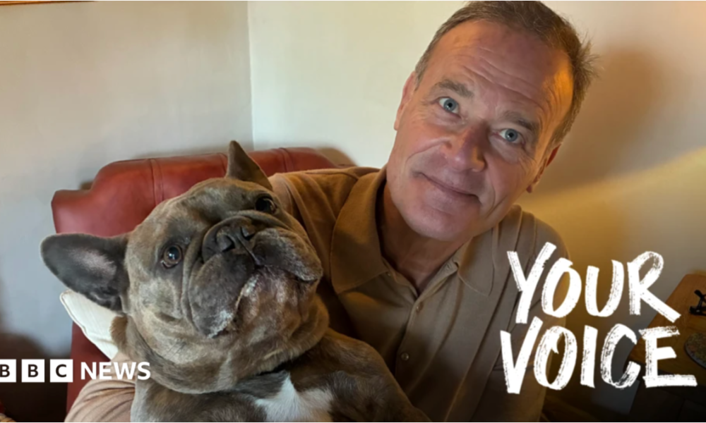 A man sat on a brown, leather chair holding up his small, brown dog.