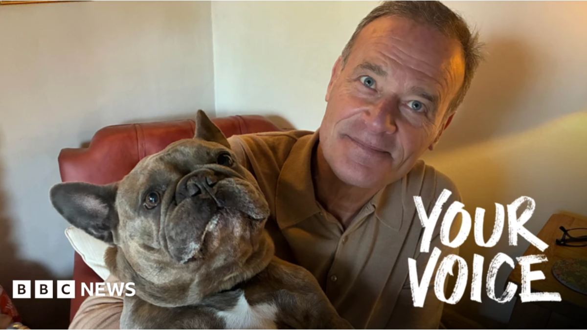 A man sat on a brown, leather chair holding up his small, brown dog.
