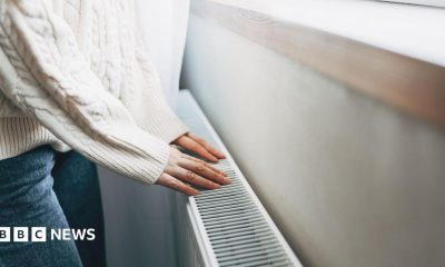 Person wearing white jumper and jeans placing their hands on a radiator.