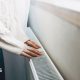 Person wearing white jumper and jeans placing their hands on a radiator.