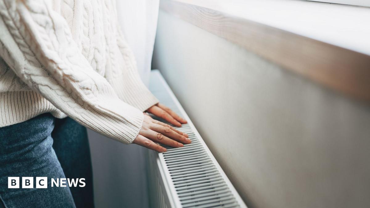 Person wearing white jumper and jeans placing their hands on a radiator.