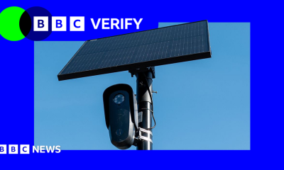 A black Flock surveillance camera attached to a pole with a solar panel attached above it