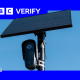 A black Flock surveillance camera attached to a pole with a solar panel attached above it