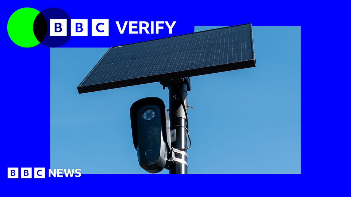 A black Flock surveillance camera attached to a pole with a solar panel attached above it