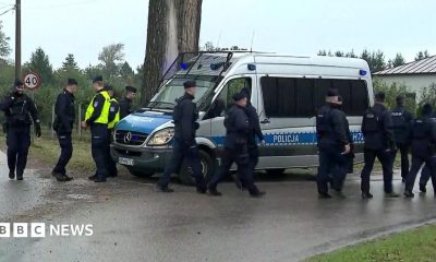 Police walk next to a silver police van near the telecommunications station in Wola Krobowska, Masovian Voivodeship province.