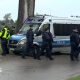 Police walk next to a silver police van near the telecommunications station in Wola Krobowska, Masovian Voivodeship province.