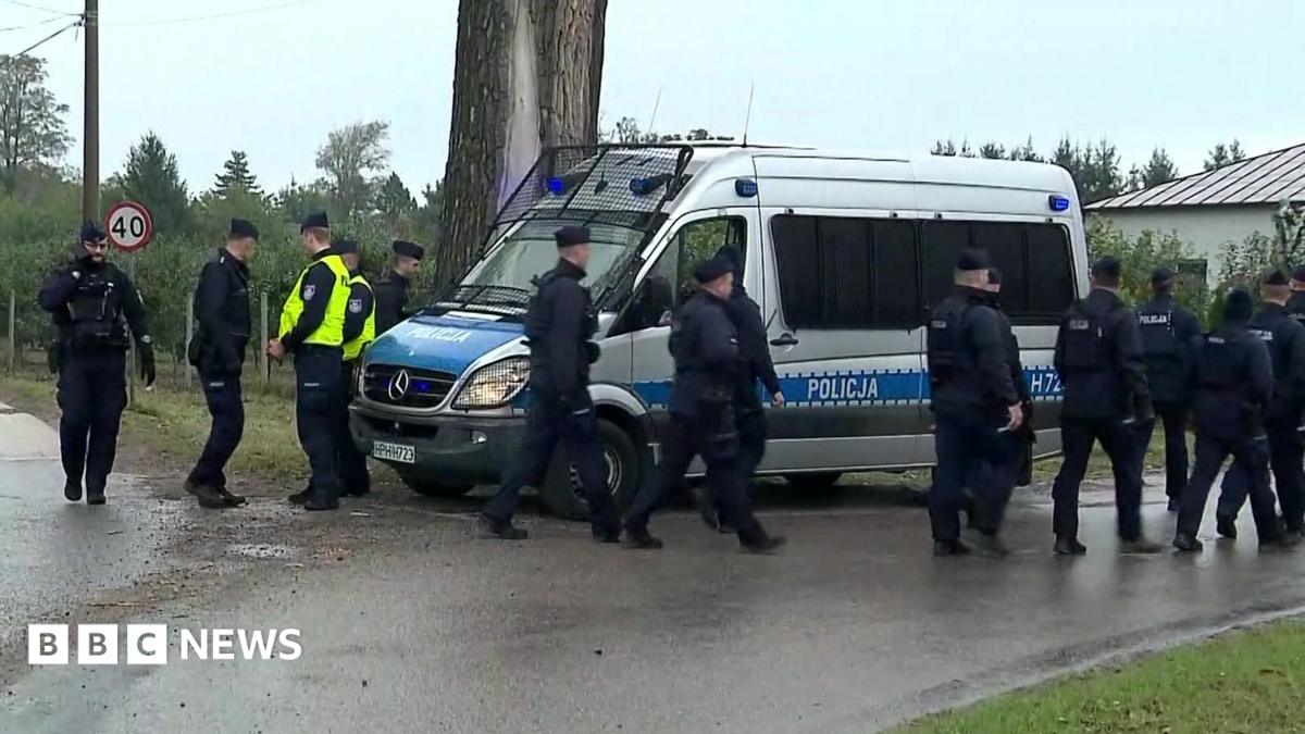 Police walk next to a silver police van near the telecommunications station in Wola Krobowska, Masovian Voivodeship province.