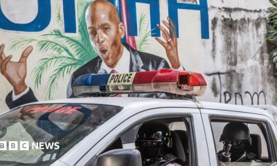 Police drive past a wall painted with the image of killed Haitian President Jovenel Moise
