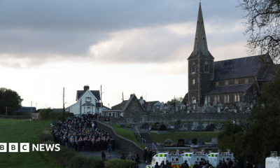 Orange Order members and their supporters gather near Drumcree Parish Church in Portadown. There are white police vehicles further down the road.