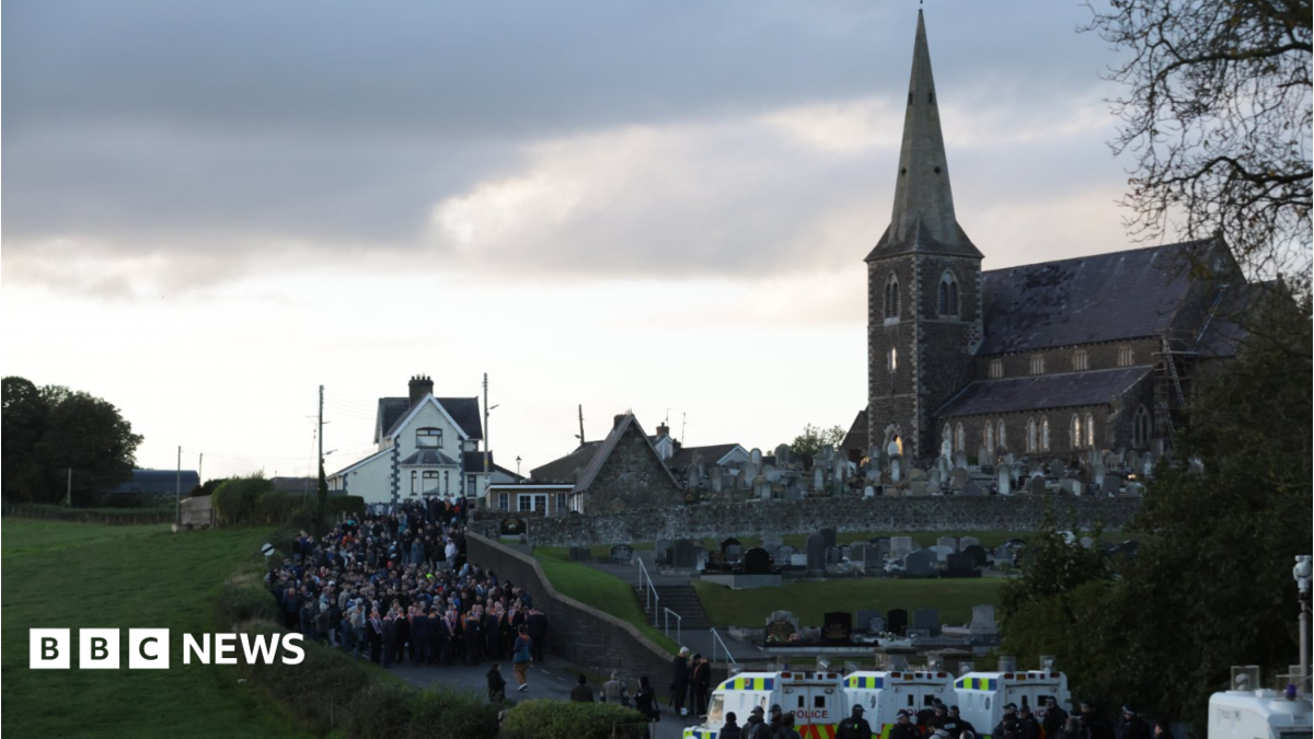 Orange Order members and their supporters gather near Drumcree Parish Church in Portadown. There are white police vehicles further down the road.