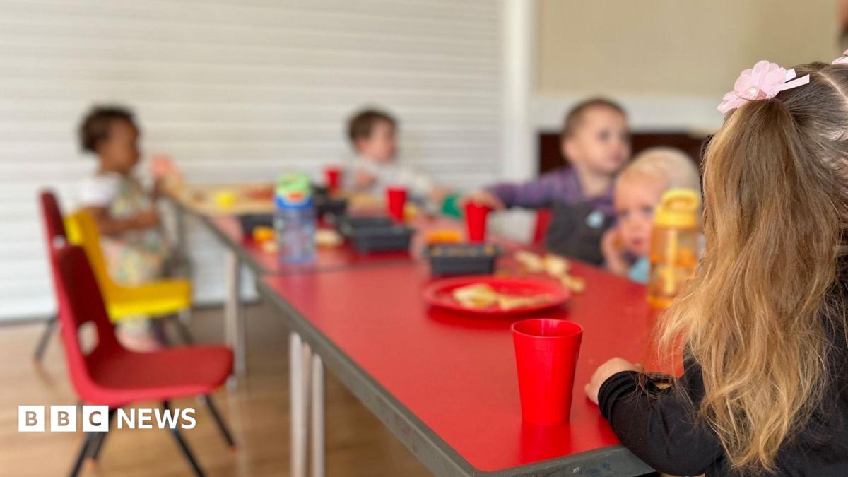 The image shows a group of unidentifiable toddlers sitting around a table eating and drinking. The table is red and the children's faces are blurry.