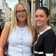 Two women stand in the street. One wears a white top, the other wears black and white.