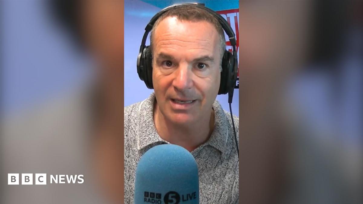 Martin Lewis looks into the camera. He is wearing headphones and is sat in front of a microphone with a blue mic muff. Only his face and shoulders are visible.