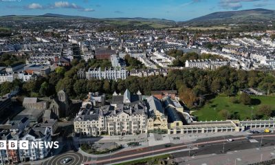 An aerial view of Douglas from the promenade on a bright day, showing hundreds of buildings with areas of trees breaking it up.