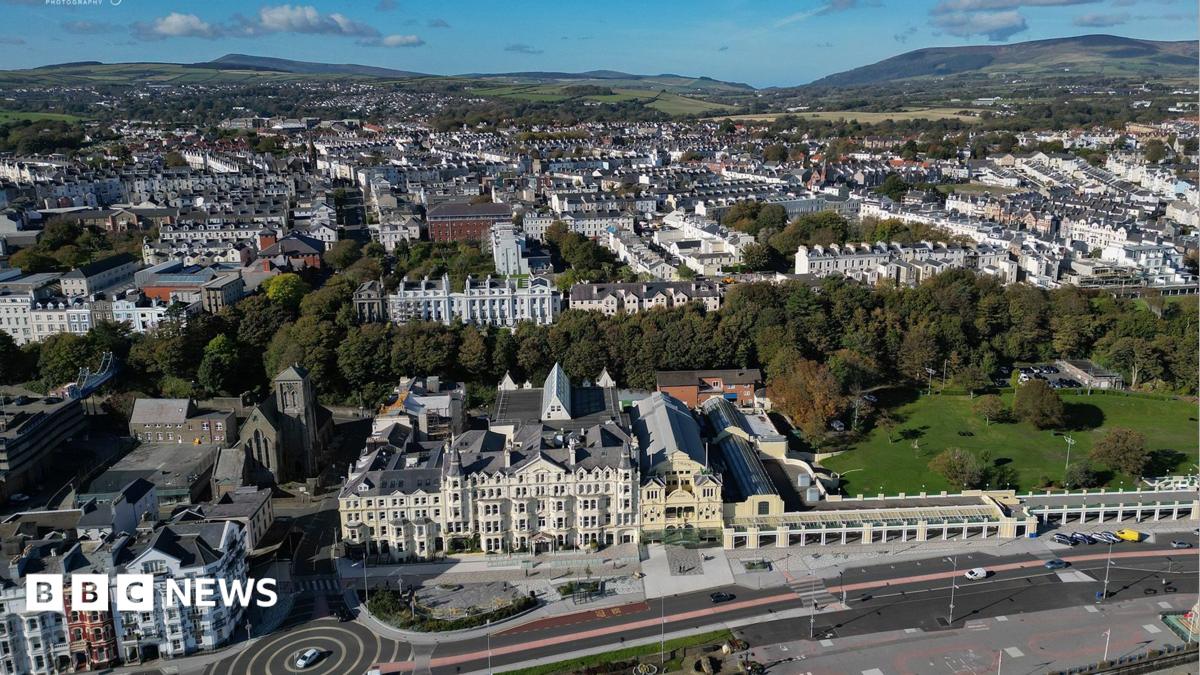 An aerial view of Douglas from the promenade on a bright day, showing hundreds of buildings with areas of trees breaking it up.
