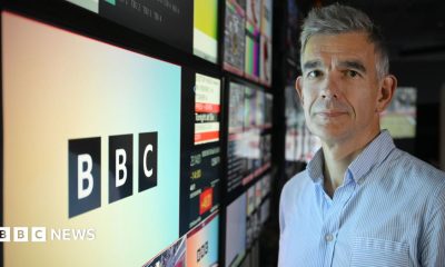Laura Kuenssberg and Matt Brittin sitting in read theatre-style seats and speaking during the interview, with a camera filming them