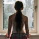 A young girl with a ponytail staring out of a window, seen from behind