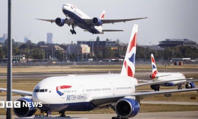Three British Airways aircraft at Heathrow Airport, one is taking off in the distance with London skyline in the background
