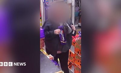 Shop customer with their face blurred putting a large chocolate bar under her jacket inside a shop