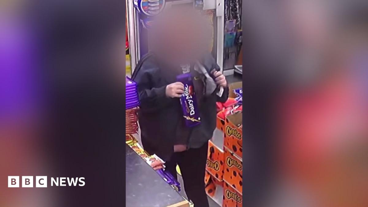 Shop customer with their face blurred putting a large chocolate bar under her jacket inside a shop