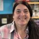 Patsy Lockerby, who has long dark hair in the ponytail and is wearing a pink, white and grey checked shirt. She'd standing behind the counter in her tearoom.