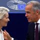 A smiling Mark Carney, wearing a suit, walks alongside European Parliament President Roberta Metsola and Ursula von der Leyen at the European Parliament