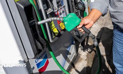 A man wearing a checked shirt and jeans returns a fuel nozzle after refueling a vehicle with diesel at a Chevron petrol station.