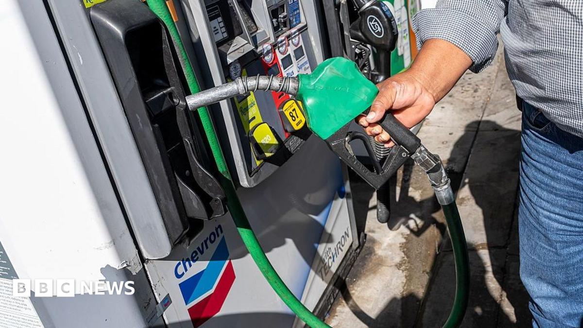 A man wearing a checked shirt and jeans returns a fuel nozzle after refueling a vehicle with diesel at a Chevron petrol station.